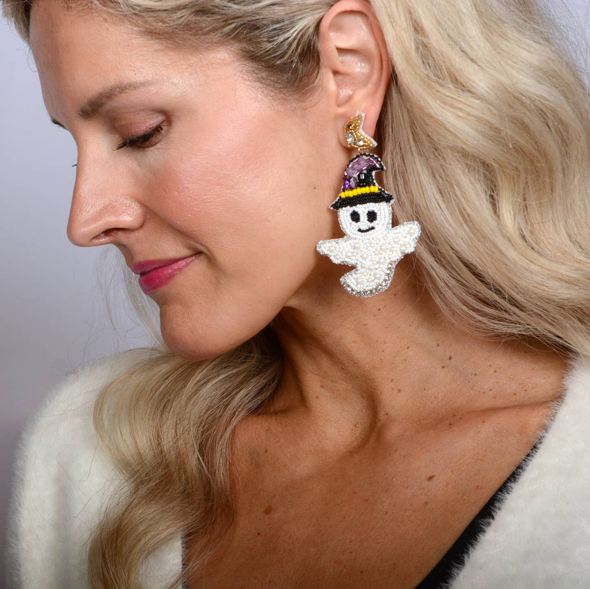 Woman wearing a large beaded ghost earring with a purple witch hat and gold moon stud.