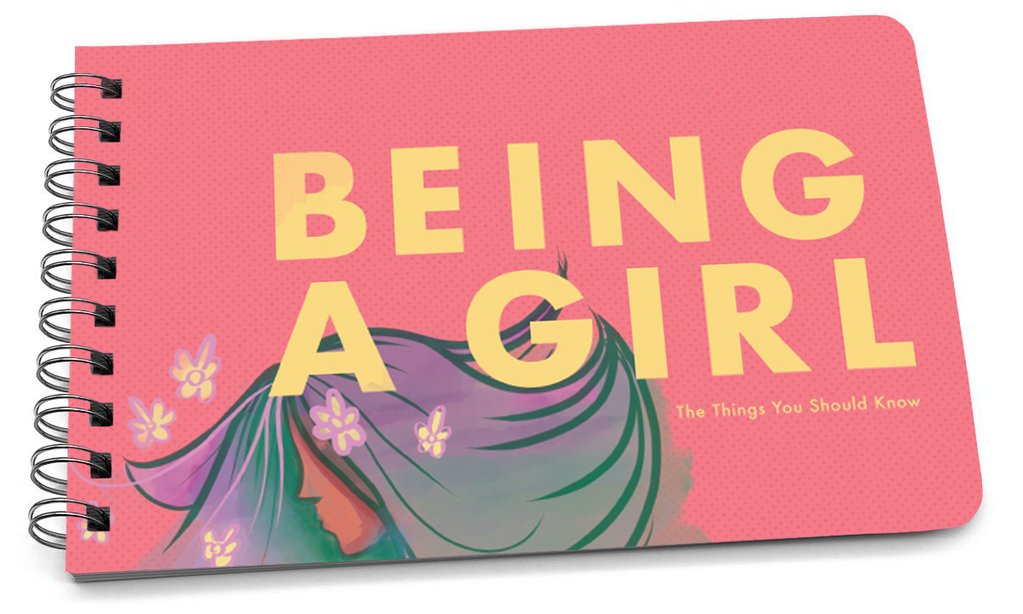 Spiral-bound handbook with a pink cover featuring the title "BEING A GIRL" in yellow letters and an illustration of a girl's profile with colorful hair.