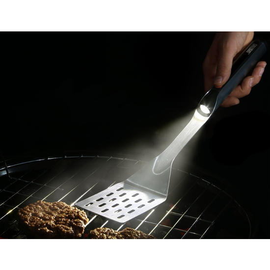 Stainless steel lighted spatula with built-in flashlight illuminating a burger on a grill.
