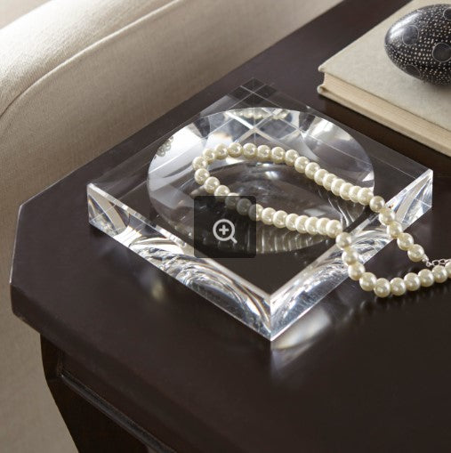 Square Luxe Bowl made of clear glass holding a pearl necklace on a dark wood table.