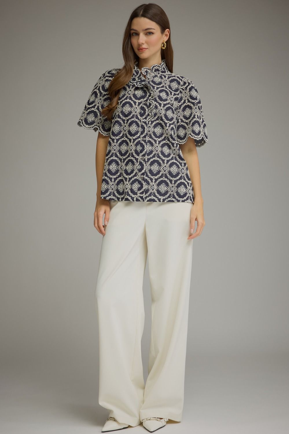 Woman wearing the Amalia navy geometric embroidered short puff sleeve top with white trousers.