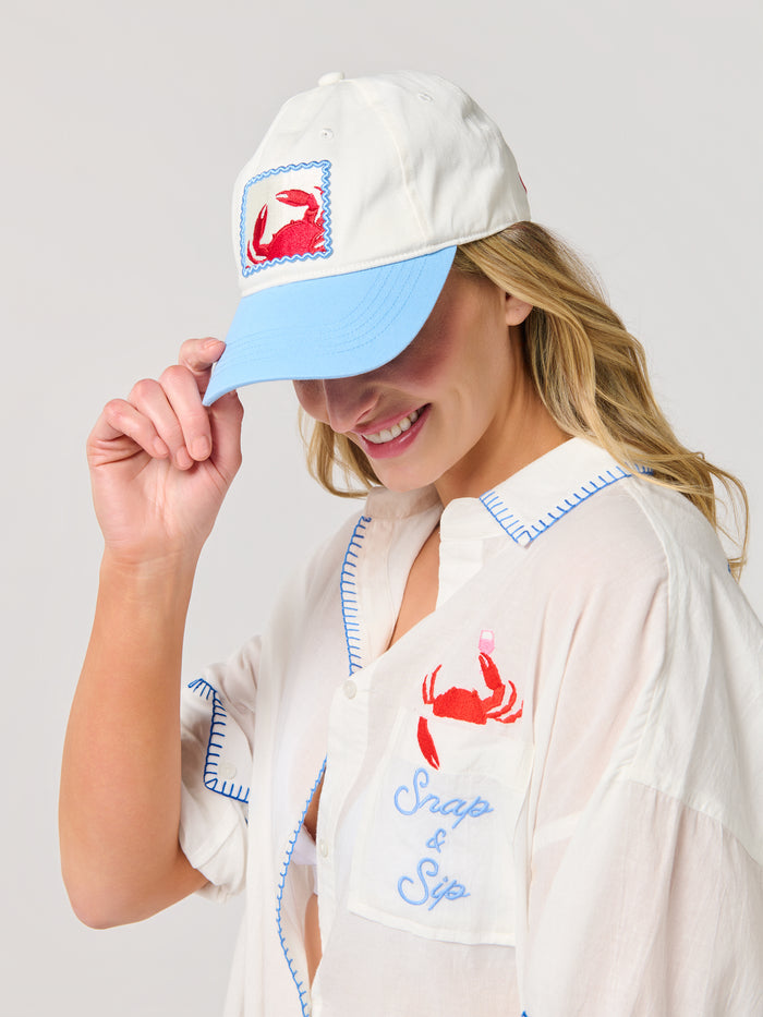 Woman wearing a white Crab Ball Cap with a red crab embroidery and a sky-blue brim.