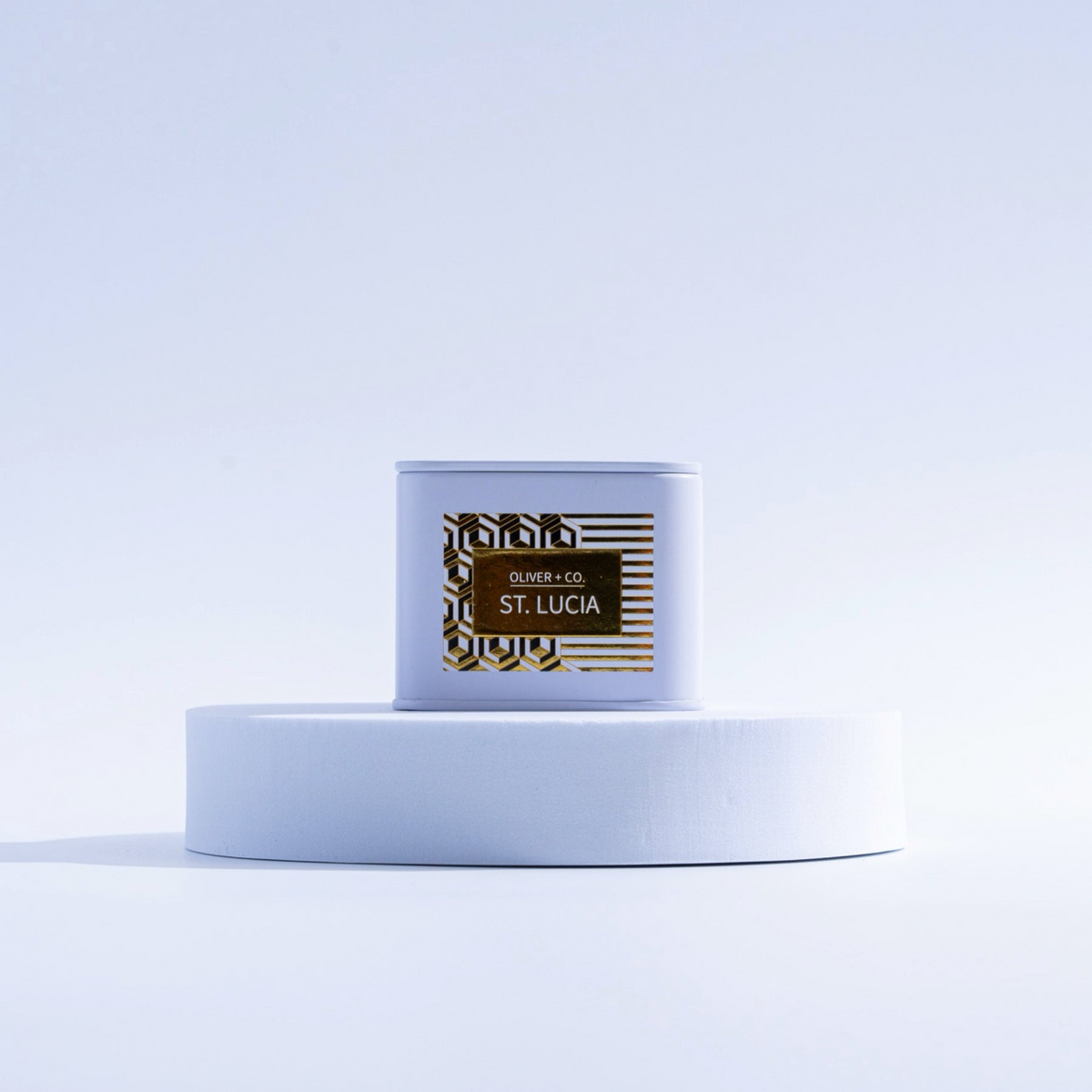 Travel Companion Candle in a white tin with gold St. Lucia label on a white circular pedestal.