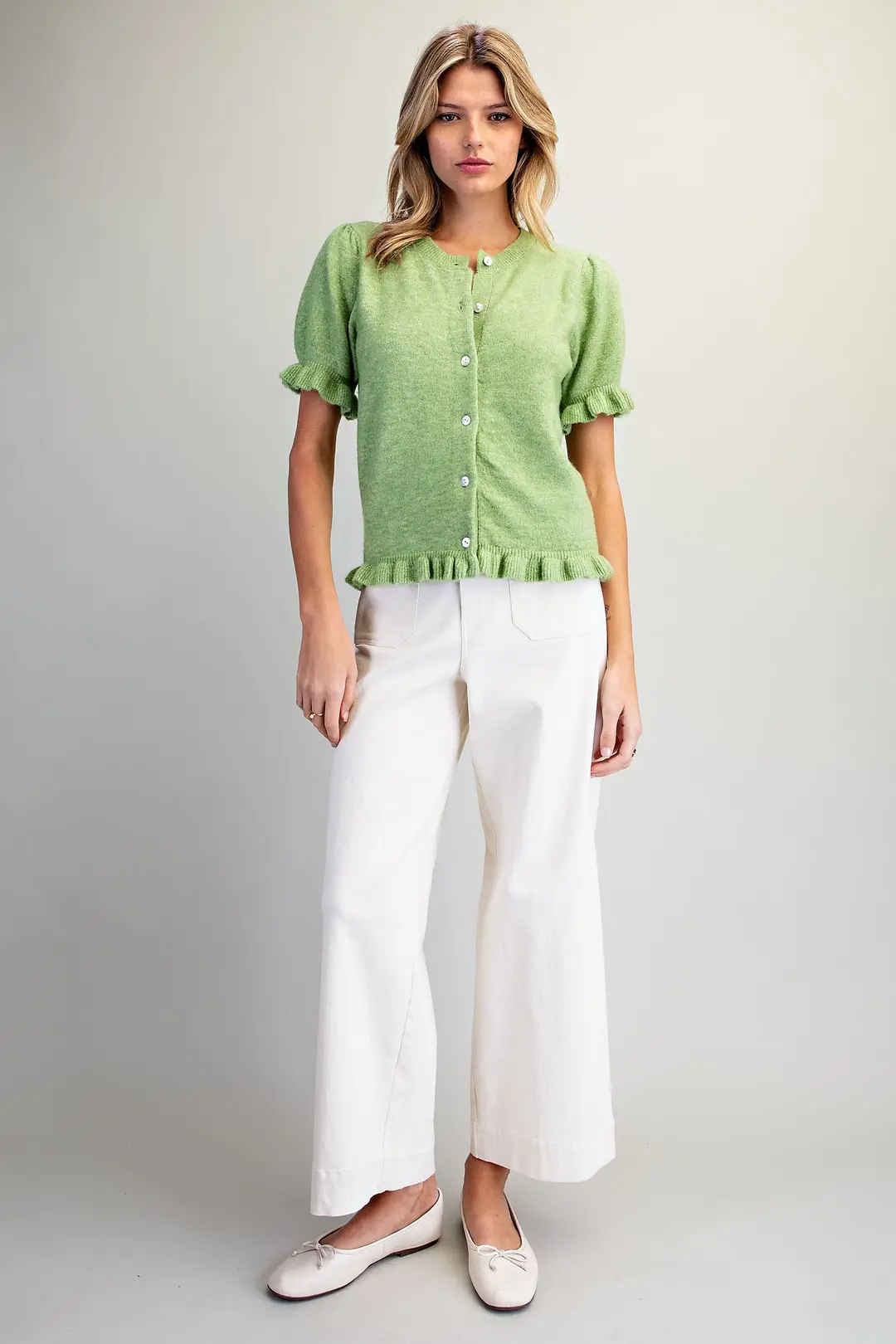 Woman wearing the Ezra green short sleeve cardigan with ruffle trim and white wide-leg pants.
