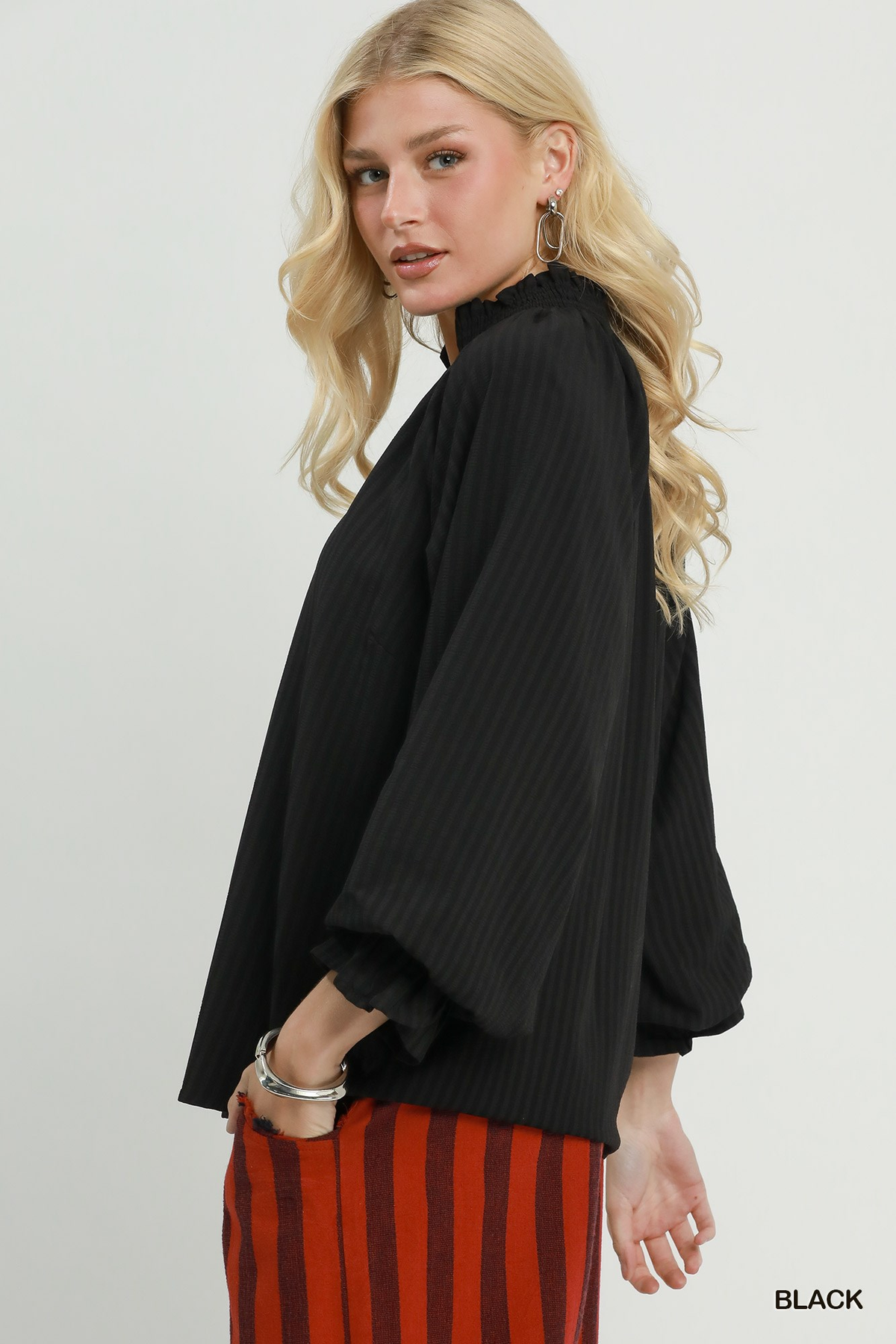 Woman wearing the black Emma Stripe Split Neck Blouse with ruffled collar and long sleeves.