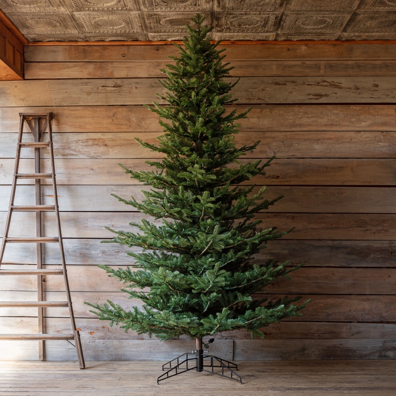 10-foot Grand Noble artificial Christmas tree with a metal stand against a rustic wooden wall.