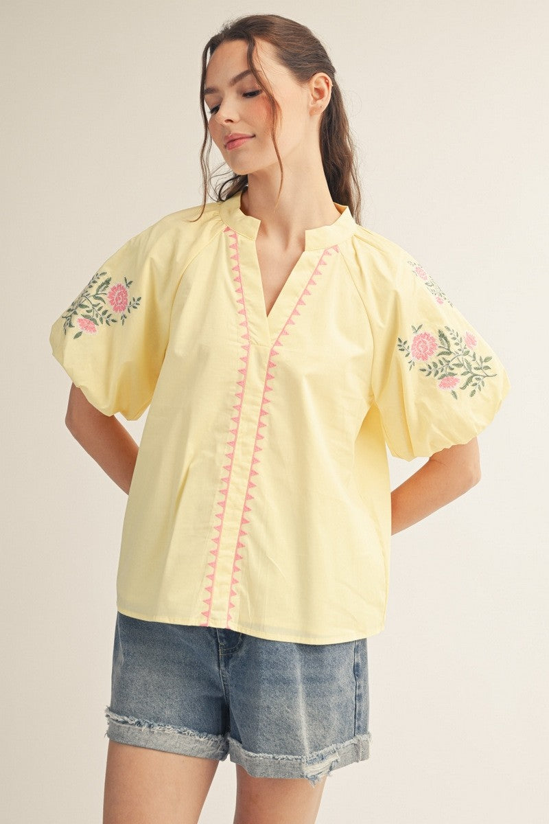 Woman wearing a Hailey yellow short puff sleeve V-neck top with pink floral embroidery and denim.