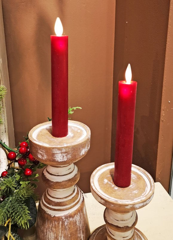 Two red moving flame LED taper candles on rustic wooden holders with holiday greenery.