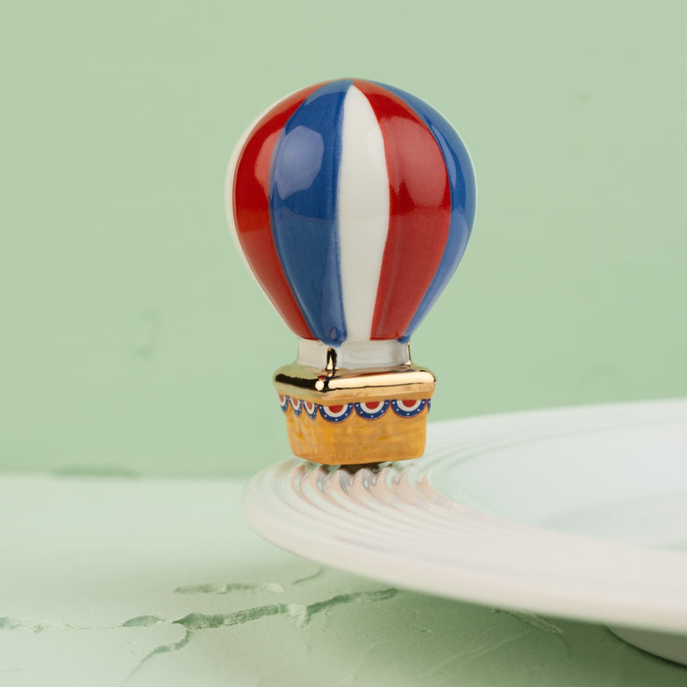 Red, white, and blue hot air balloon decorative mini on the edge of a white ceramic plate.
