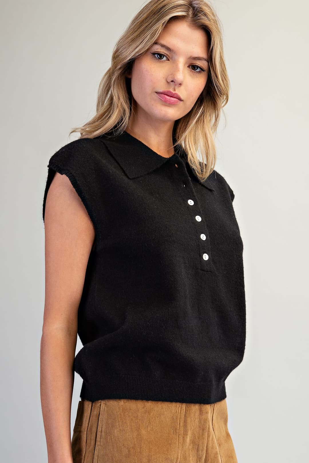 Woman wearing a black Lily Polo Collar Cap Sleeve Knit Top with white buttons and tan corduroy pants.