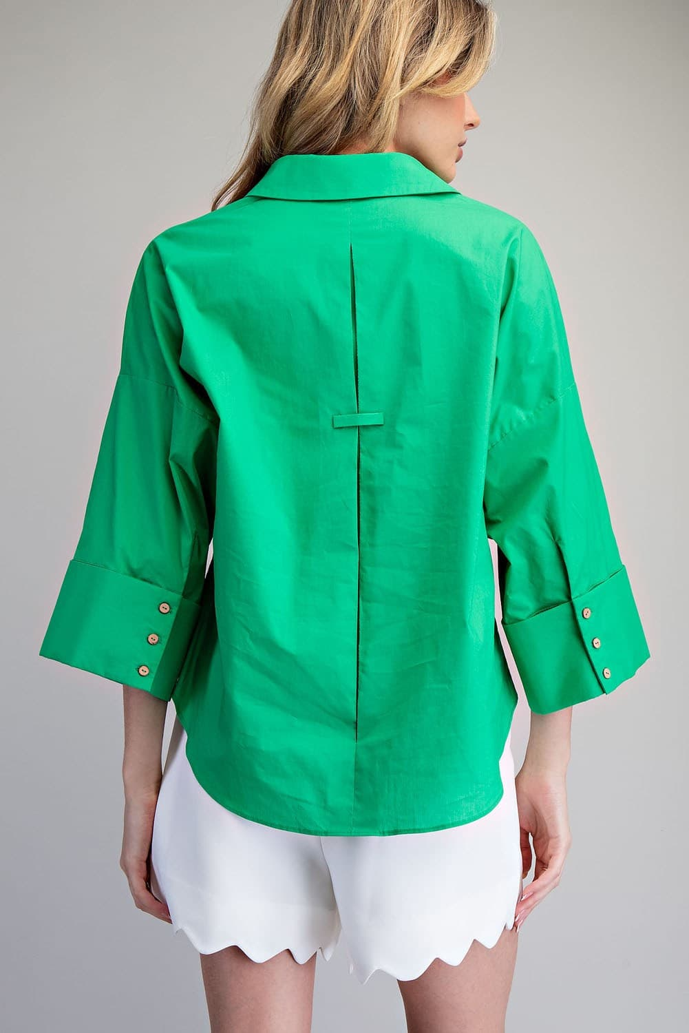 Back view of a woman wearing a green Blake button-down blouse with a center back pleat detail.