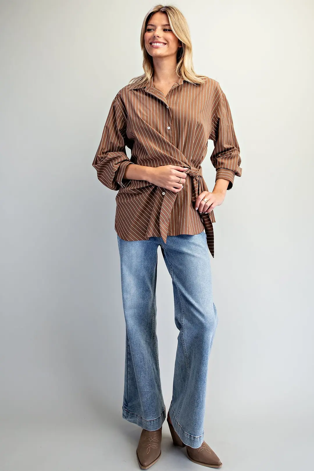 Woman wearing a brown Reese pinstriped blouse with a tie waist front and blue wide-leg jeans.