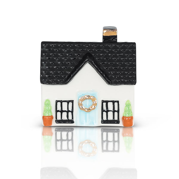 Miniature white house with black roof, blue door with wreath, and two potted plants.