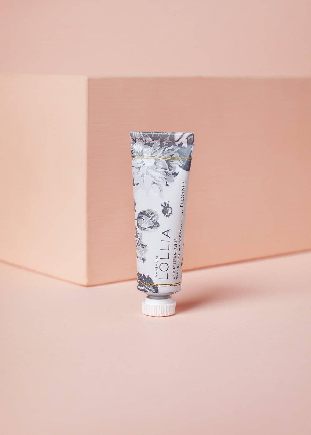 Lollia Elegance Petite Treat Handcreme tube with grey floral pattern on a peach background.