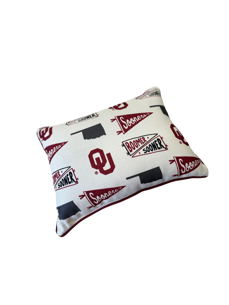 Oklahoma Sooners collegiate cluster pillow with crimson piping and team logos on white fabric.