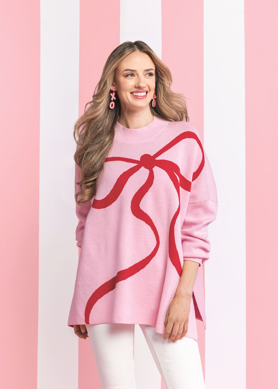 Woman wearing a pink Valentine's Jacquard Sweater with a large red bow design and white pants.