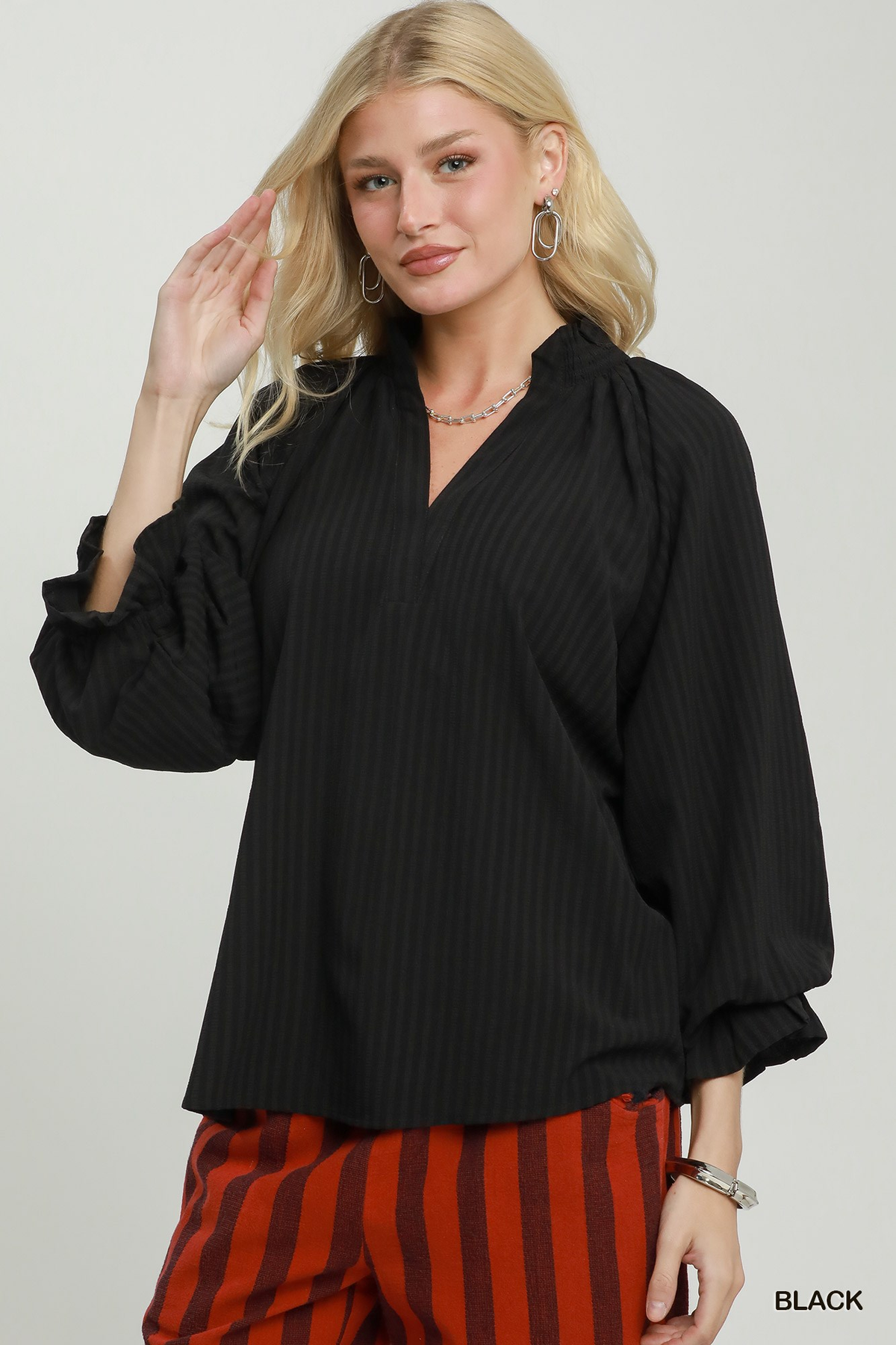 Woman wearing the Emma Stripe Split Neck Blouse in black with a ruffled collar and long sleeves.