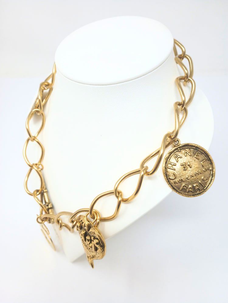 Gold link necklace featuring five charms: Paris heart, Eiffel Tower, number five, and two Chanel-style coins.