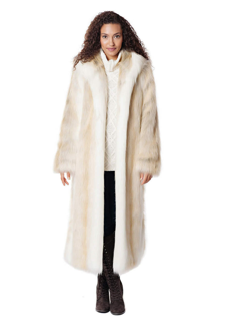 Woman wearing a long, hooded faux fur coat in white and tan over a white sweater and dark boots.