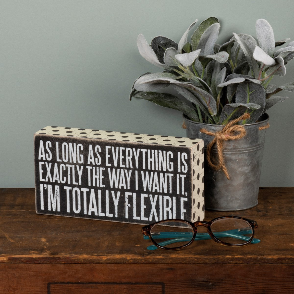 Wooden box sign with black polka dots and white text reading "AS LONG AS EVERYTHING IS EXACTLY THE WAY I WANT IT, I'M TOTALLY FLEXIRI F."