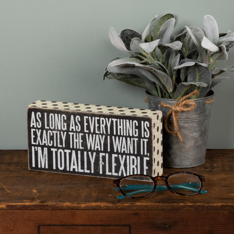 Wooden box sign with black polka dots and white text reading "AS LONG AS EVERYTHING IS EXACTLY THE WAY I WANT IT, I'M TOTALLY FLEXIRI F."