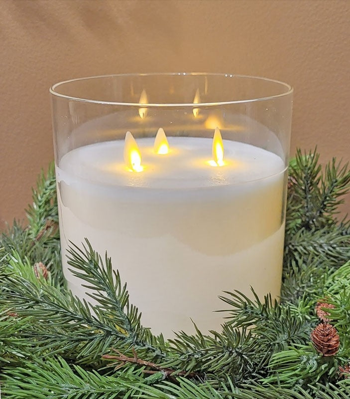 A 6x6 glass 3-wick flameless candle with glowing LED wicks set in a green pine wreath.