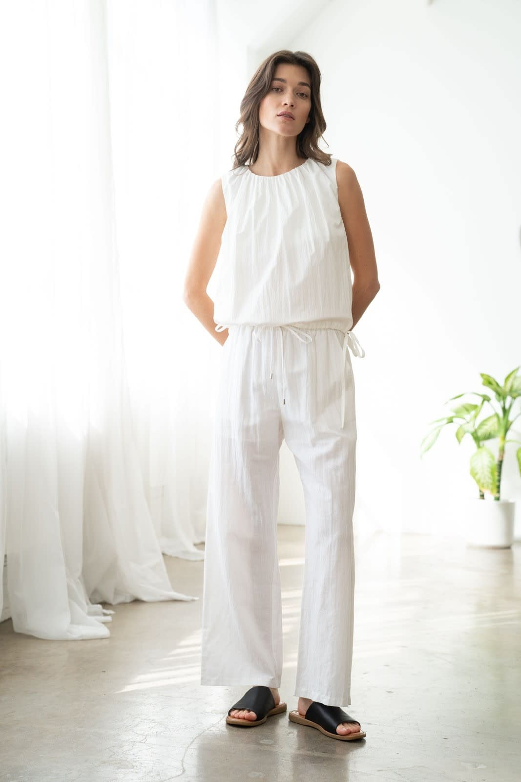 White linen pants with elastic waistband, side pockets, and wide-leg straight silhouette.