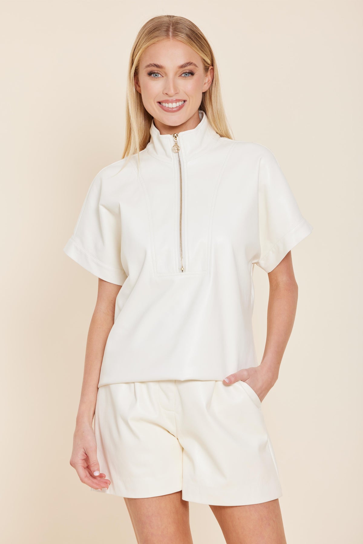 Woman wearing the Angela white faux leather short sleeve top with a gold quarter-zip and high neck.
