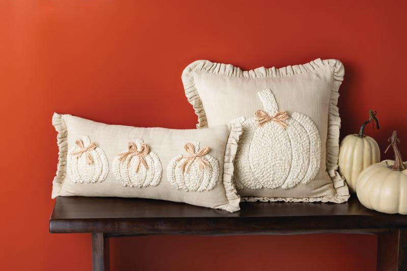 Square white chambray pillow with embroidered pumpkin yarn detail, ruffle flange, and raffia bow accent.