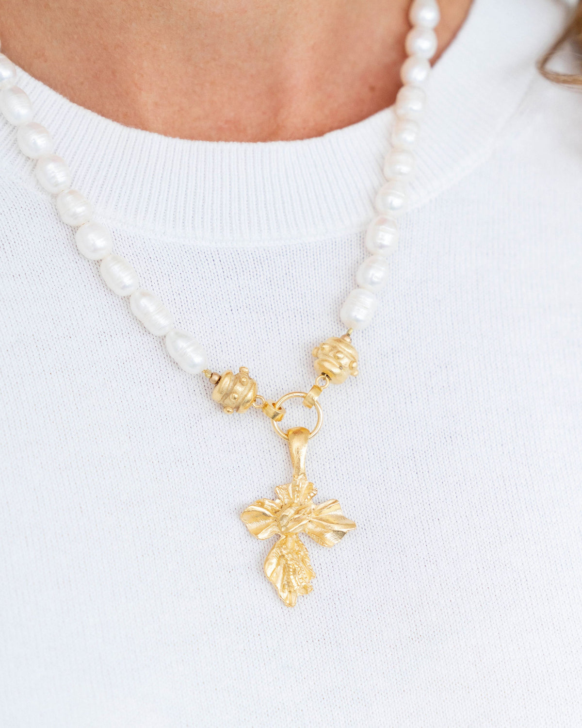 Gold vintage cross pendant on a genuine freshwater pearl necklace worn over a white shirt.