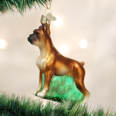 Glass boxer dog Christmas ornament with brown coat and white chest standing on a green base.
