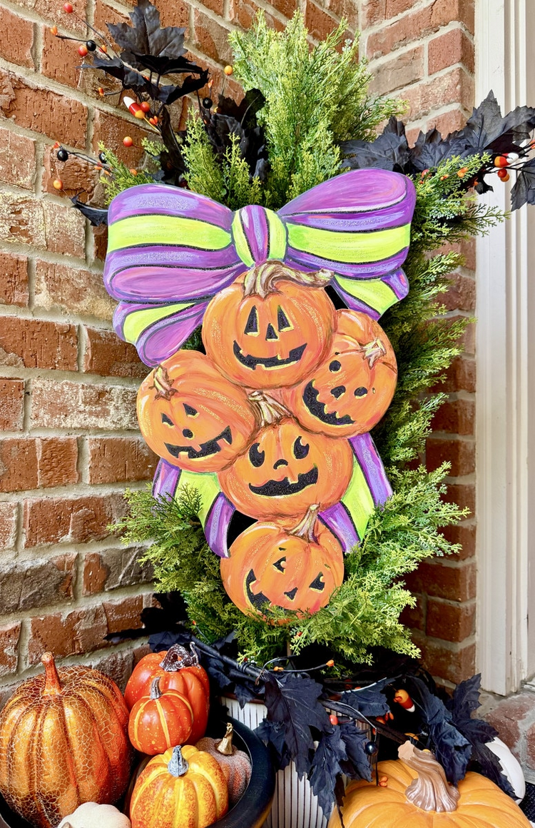 Metal Jack O Lantern Swag featuring five carved pumpkins and a purple and green bow on greenery.