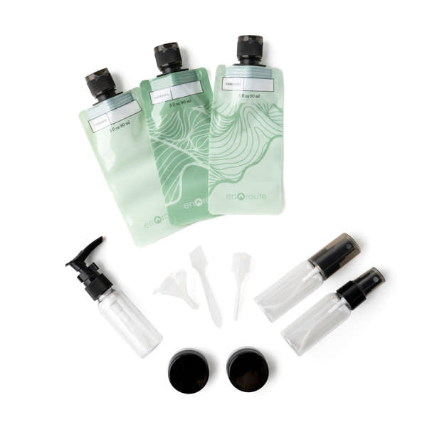 Green reusable travel kit with squeeze pouches, spray bottles, pump bottle, mini jars, dropper, funnel, and scraper.