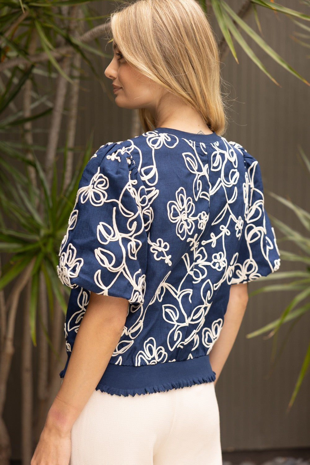 Natty floral embroidered woven top with short bubble sleeves, round neckline, ruffled hem, and relaxed silhouette.