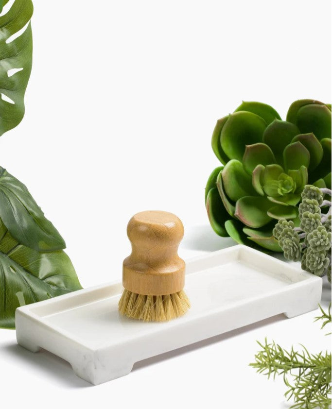 White marble sink caddy tray holding a wooden scrub brush with natural bristles.