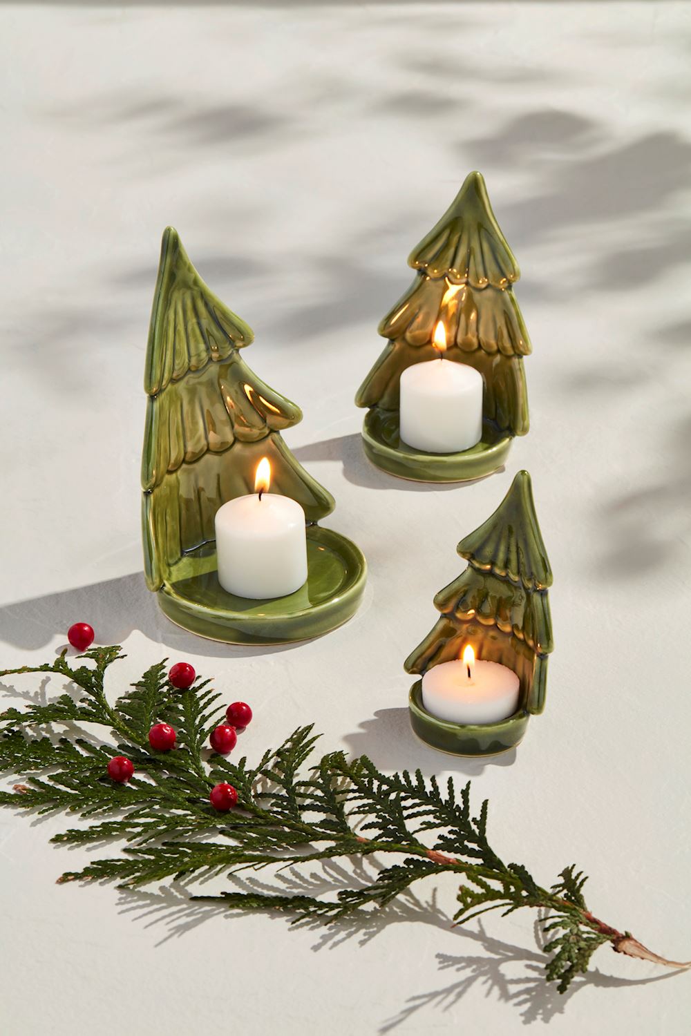 Set of three green stoneware Christmas tree votive candle holders with lit white tea lights.