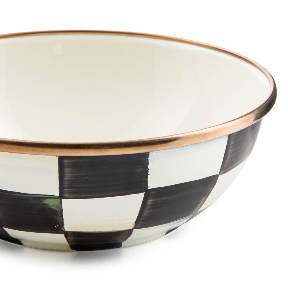 Close-up of a hand-painted black and white checkered enamel bowl with a bronzed stainless steel rim.