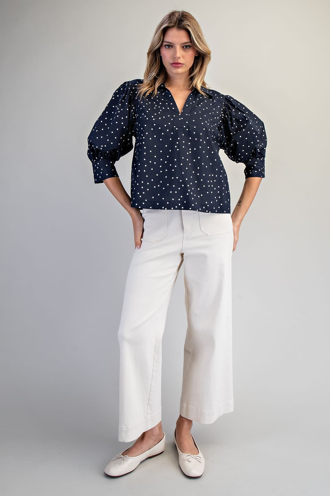 Woman wearing a navy Molly Polka Dot Puff Sleeve Blouse with white wide-leg pants and ballet flats.