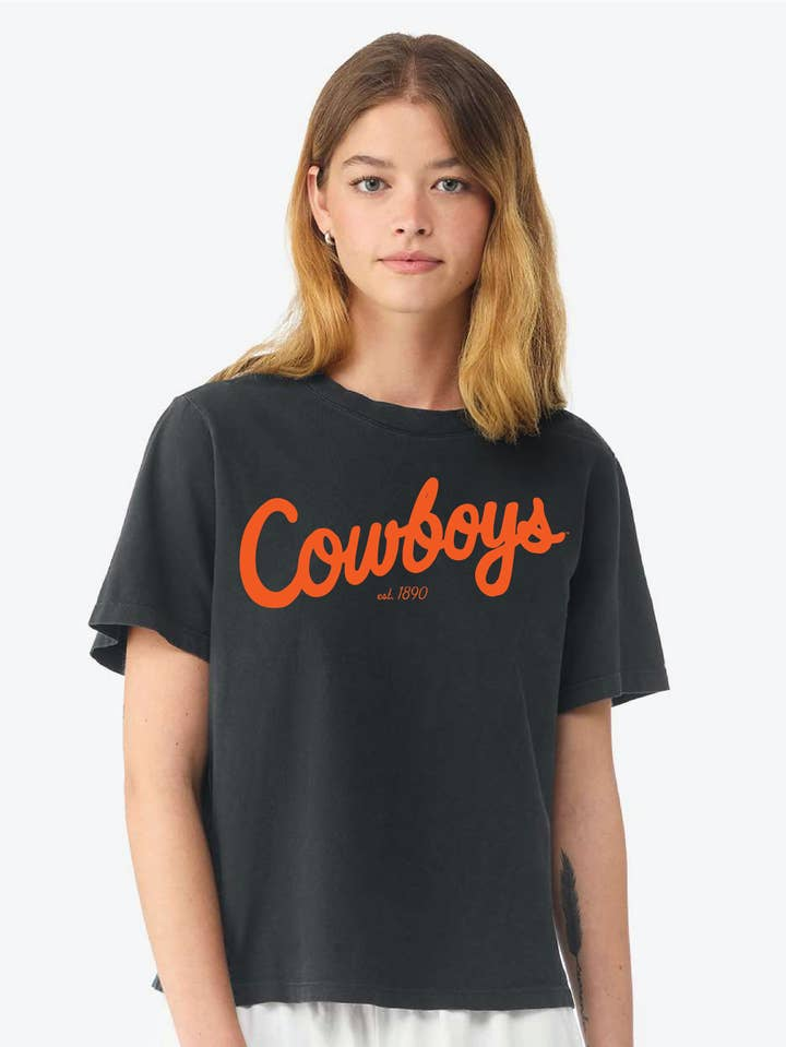 Woman wearing a black Cathy Osu Cowboys Bold Script Ellie Heavyweight Tee with orange script.