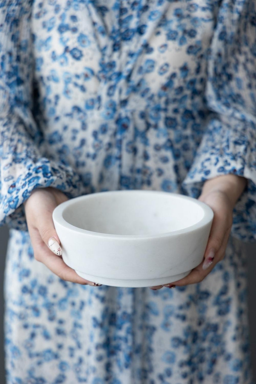 A person holding a solid white marble bowl with a tiered base design.