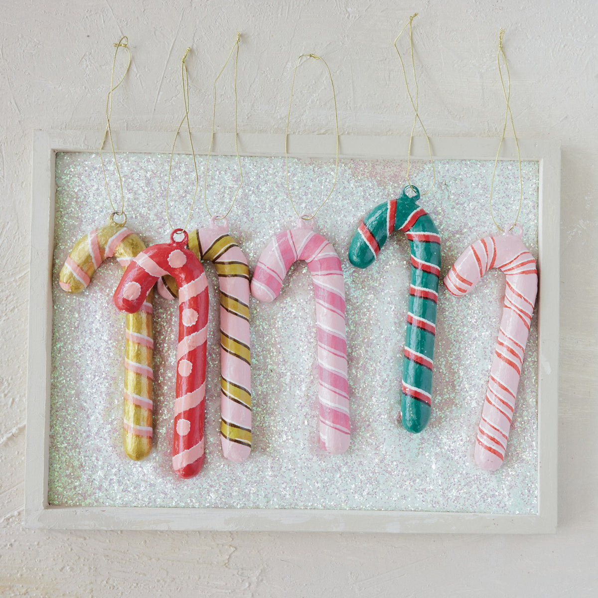 Six colorful, handcrafted metal and paper mache candy cane ornaments with various striped patterns.