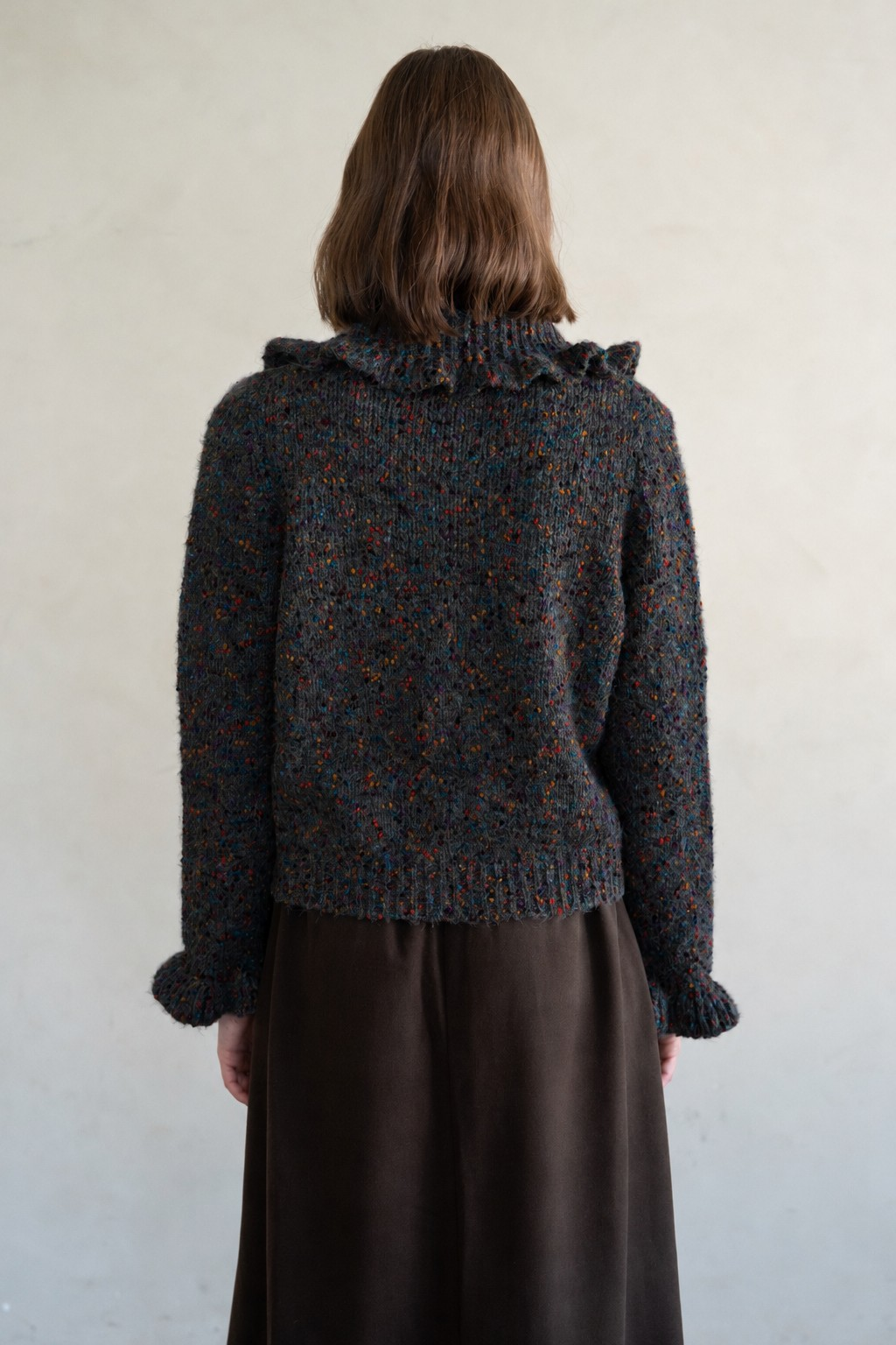 Back view of a person wearing the Amanda Flecked Ruffle Collar Cardigan in dark grey with colorful flecks.