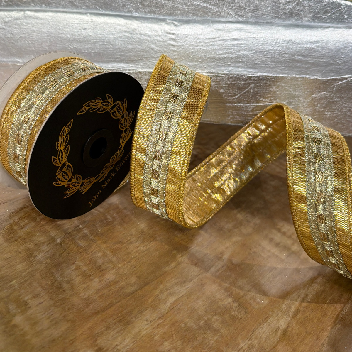 A spool of 1.5-inch wide gold metallic dupion ribbon with an ornate woven center trim.
