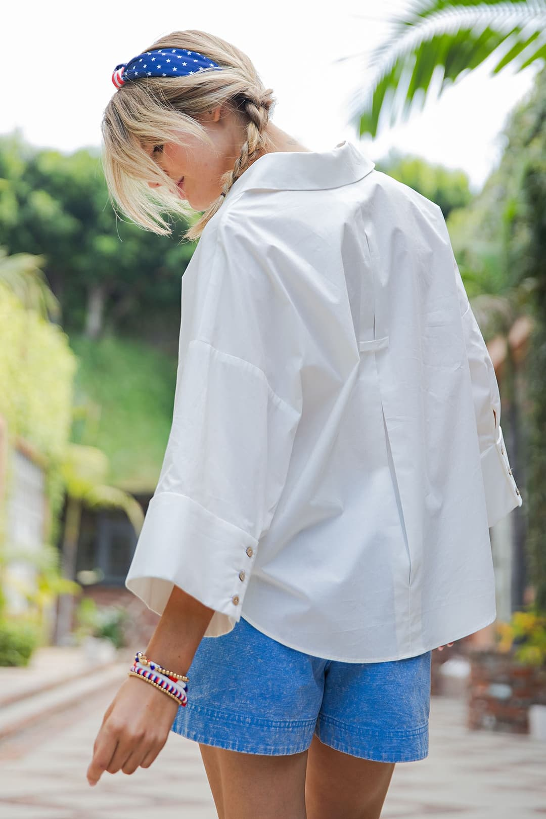 Woman wearing a white Blake Back Pleat Button Down Blouse with blue shorts and a headband.