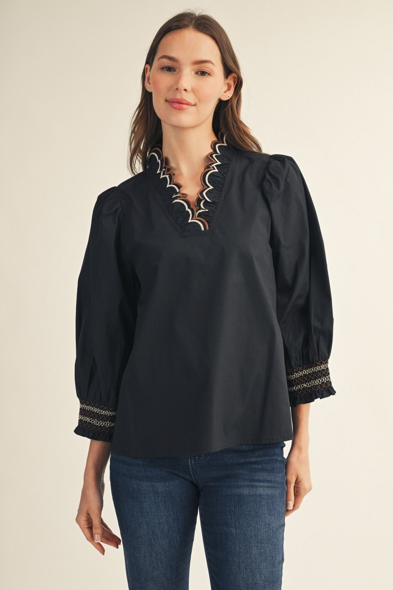 Woman wearing a black Millie top with embroidered scallop V-neckline and puff sleeves.