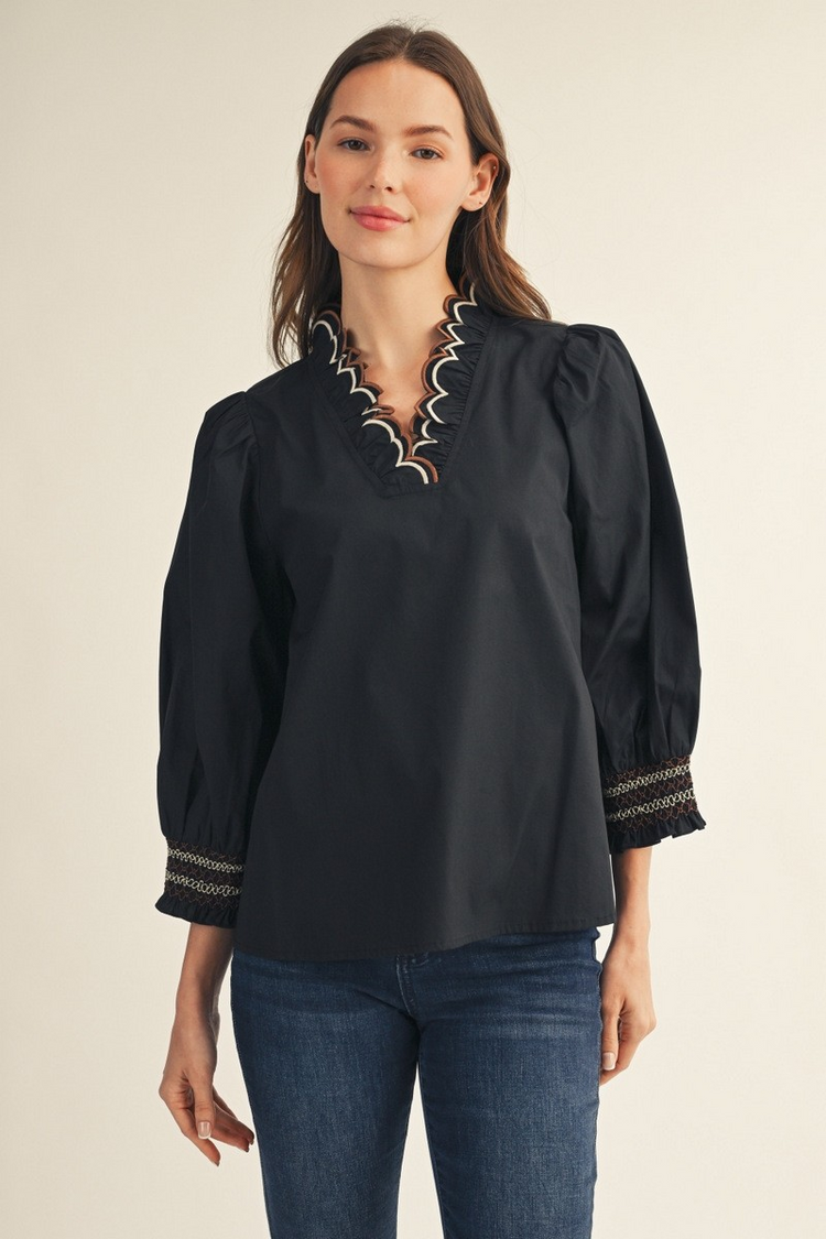 Woman wearing a black Millie top with embroidered scallop V-neckline and puff sleeves.