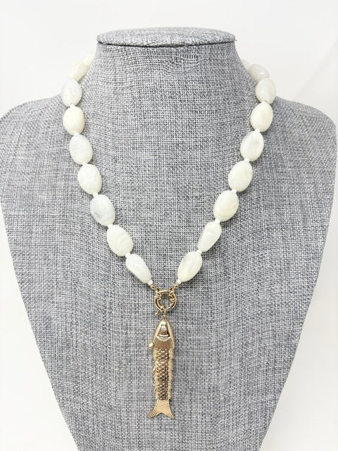A beaded necklace with smooth white oval beads and a gold fish pendant on a gray display bust.