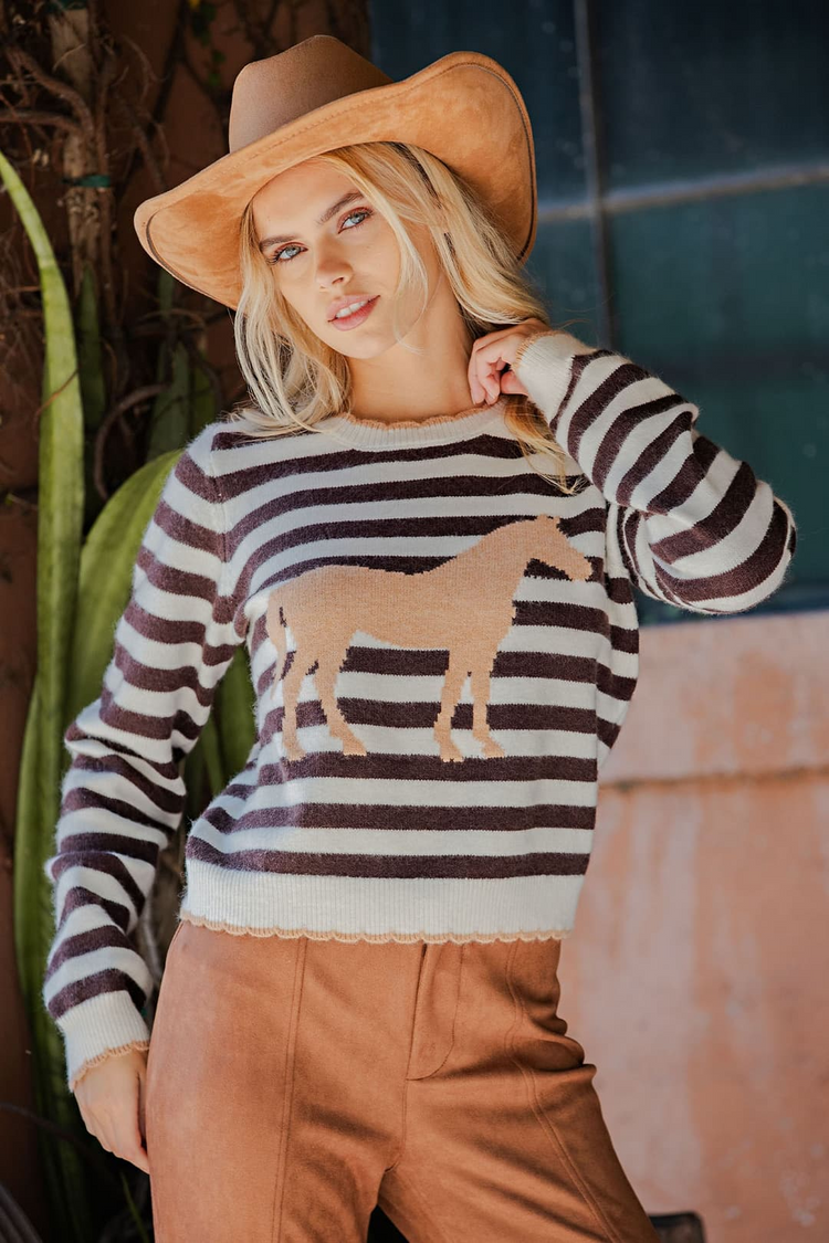 Woman wearing the Ailany brown and white striped sweater with a tan horse graphic and scallop edges.