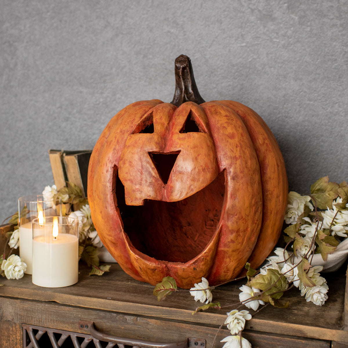 15-inch orange mache big mouth pumpkin luminary with a carved face on a wooden shelf with candles.