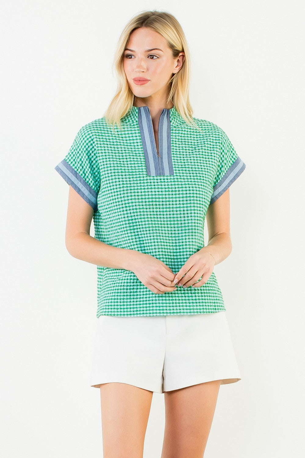Woman wearing the Ariana green and white gingham short sleeve top with a blue striped zip neckline.